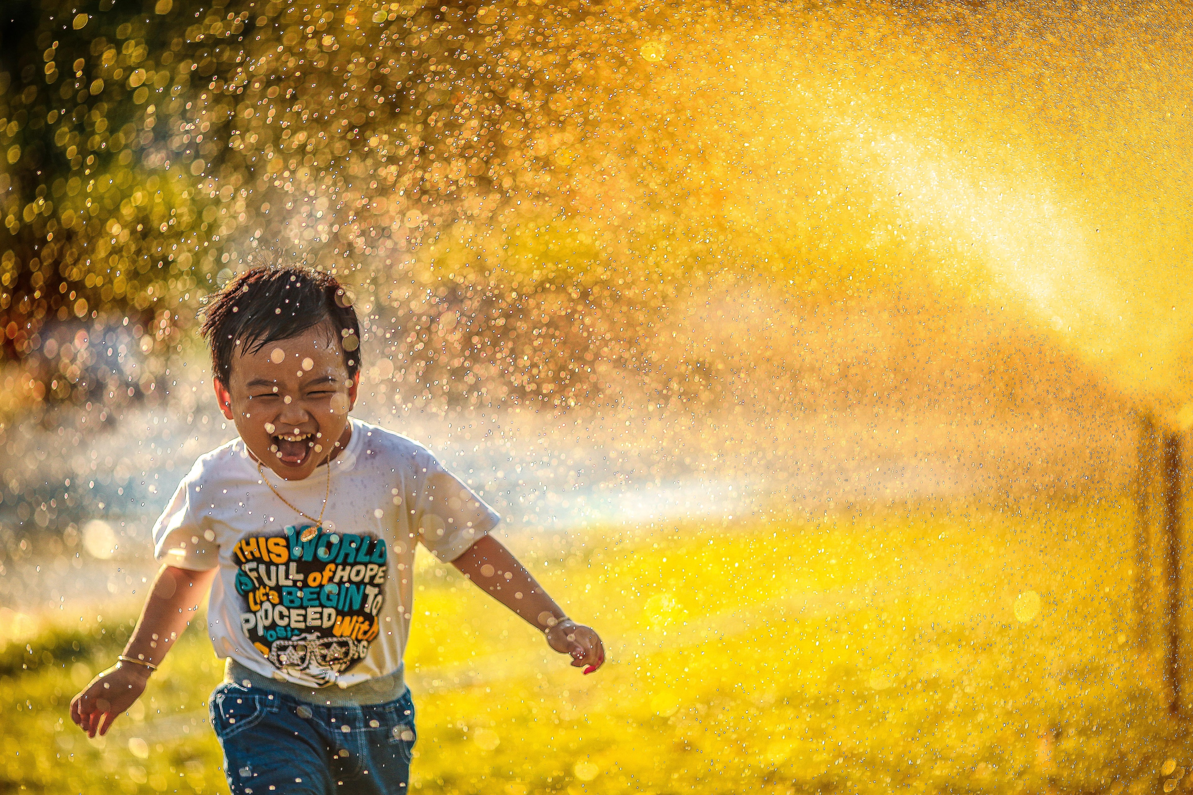 A child laughing and running through a sprinkler